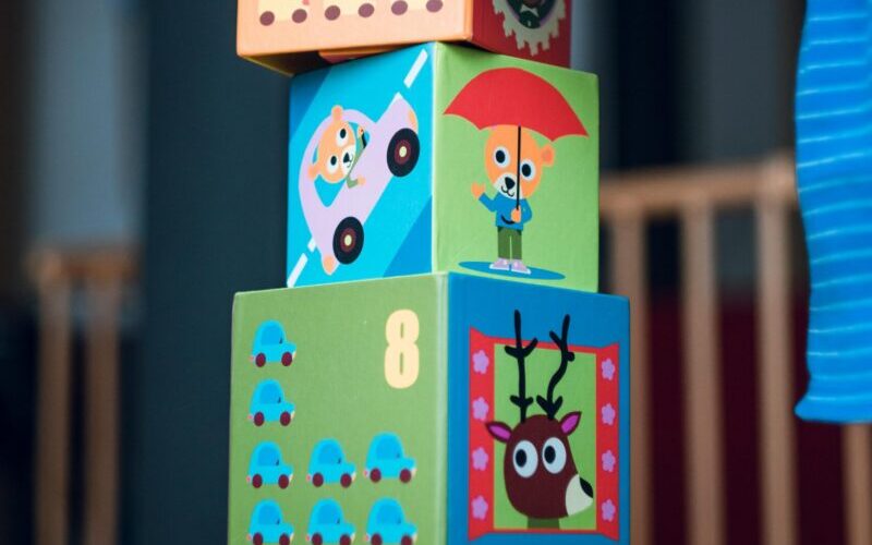 A child playing indoors, stacking colorful wooden toy blocks with joyful illustrations.