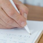 A close-up of a doctor's hand writing notes with a ballpen on paper.