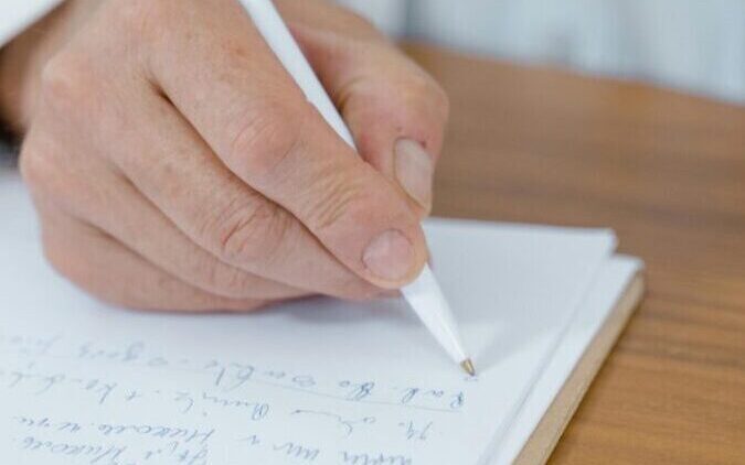 A close-up of a doctor's hand writing notes with a ballpen on paper.