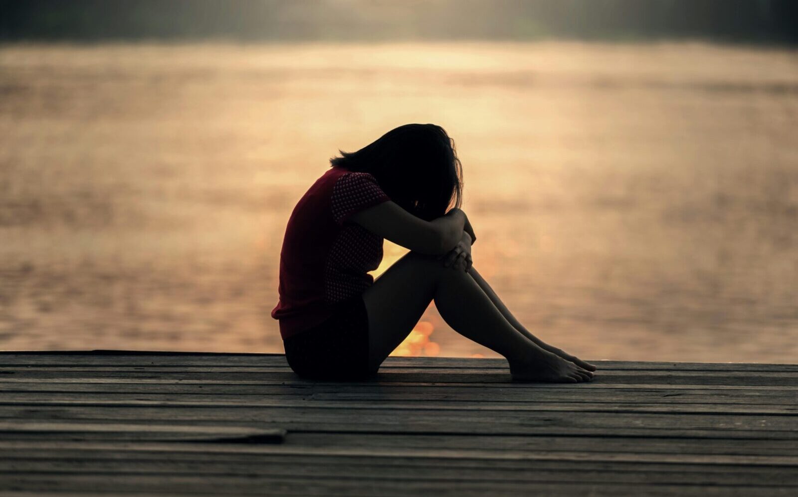 A woman sitting alone on a wooden dock by the lake, showing solitude and reflection.
